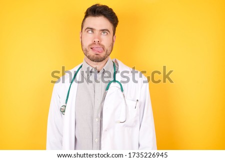 Young handsome doctor man, making grimace face crossing her eyes and showing tongue isolated over white background. Being funny and crazy