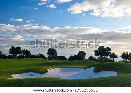 The perfect place for golf surrounded by green trees, golf course with a big hole, blue sky with clouds