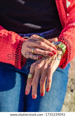 Elderly women's hands touch the wrist watch. Woman in jeans and red shirt check time on gold watches. Elegant woman hand, wrist.  Concept of time, trend, fashion, hurry up, waiting, style.