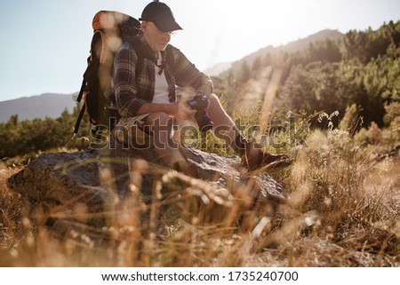 Hiker looking at pictures on digital camera during hiking. Senior man taking a break on a hike to looking at photos.