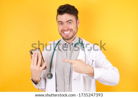 Portrait of handsome European doctor man wearing medical uniform holding in hands showing new cell, wearing yellow shirt standing against yellow background