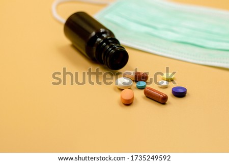 A three-layer medical mask with rubber ear straps,  a various medicines, a jar of pills. The concept of medicine, timely vaccination and health, Conceptual image of capsules and bottles with empty spa