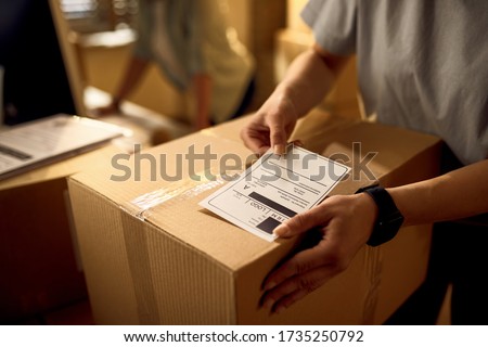 Close-up of courier attaching address label on a package while working in the office. Royalty-Free Stock Photo #1735250792