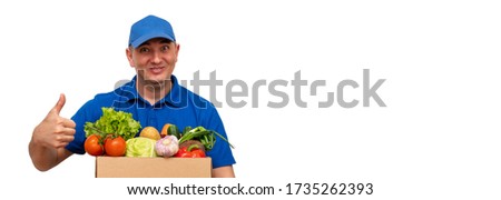 Cheerful delivery man of fresh vegetables in a blue uniform on a white background. Pointing up.