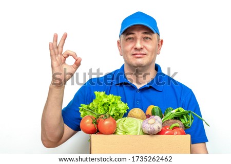 Cheerful delivery man of fresh vegetables in a blue uniform on a white background.
