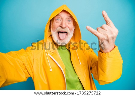 Self-portrait of his he nice cheerful cheery crazy naughty grey-haired man wearing yellow topcoat having fun showing horn symbol party isolated on bright vivid shine vibrant blue color background