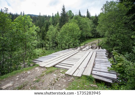 Mountain landscape, road and wooden simple bridge over a stream, river.