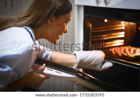 Homemade dessert. Cheerful woman taking fresh pie from oven at kitchen Royalty-Free Stock Photo #1735303595