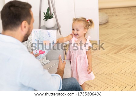 Happy Father's Day Concept. Little girl giving drawing with Daddy and Me text to father, copy space