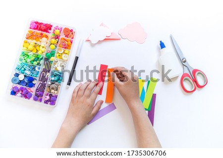 Bookmark for a child book to school. Origami paper craft with children's hands. Bright rainbow from the cloud