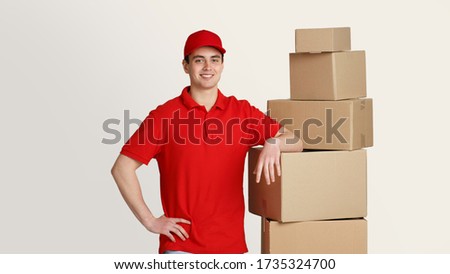 Mail worker. Smiling courier stands in storage warehouse and puts hand on boxes, studio shot