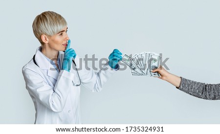 Corruption in medicine concert. Woman doctor in medical gloves takes money from patient hands and makes sign of silence, studio shot