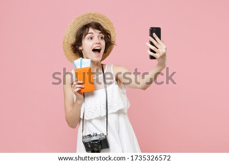 Excited tourist girl in dress hat with photo camera isolated on pink background. Traveling abroad weekend getaway. Air flight journey concept. Hold passport tickets doing selfie shot on mobile phone