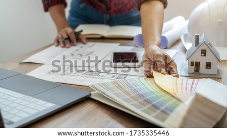 Interior designer choosing color in color swatch samples chart for house coloring selection in office with blueprint. Construction concept.