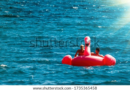 Couple having fun on pink flamingos at blue sea. Sunset holiday travel vacation background with funny flamingo toy float header as romantic couple background, exotic love romance destination.