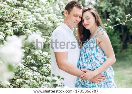 Young parents walk in the park on a warm spring day. Pregnant young woman in nature. Happy future parents. Waiting for a miracle.