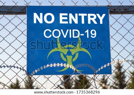 The inscription "NO ENTRY COVID-19" on a blue plate on an iron mesh fence rewound with barbed wire. Closed area. Quarantine and lockdown concept