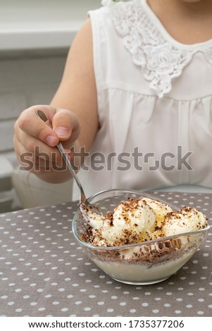 a bowl with vanilla ice cream sprinkled with chocolate on the kitchen table. the child took a spoon and is going to eat it
