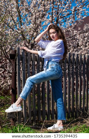 Full body portrait of a young stylish girl in in blue jeans against the background of blooming cherry