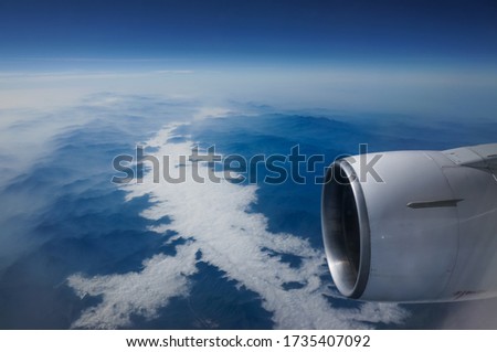 A foggy blue sky with a white cloud pattern and  viewing from airplane's window near jet turbine engine on high altitude above the montain