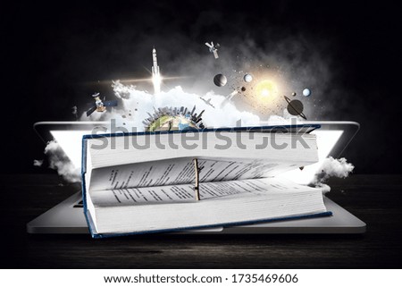 Laptop with book, planet and space on dark background