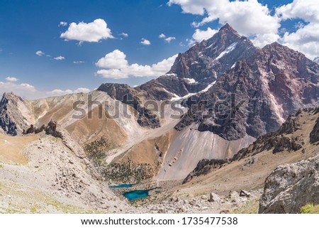 The beautiful mountain trekking road with clear blue sky and rocky hills and the view of Alaudin lake in Fann mountains in Tajikistan