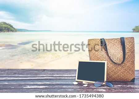 bamboo bag and chalkboard on wooden floor over blurred tropical beach and blue sea