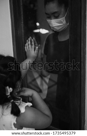 Mother wear face mask meeting daughter and touching hand through the window because of the quarantine Corona Virus Covid-19, social distancing, Black and white picture