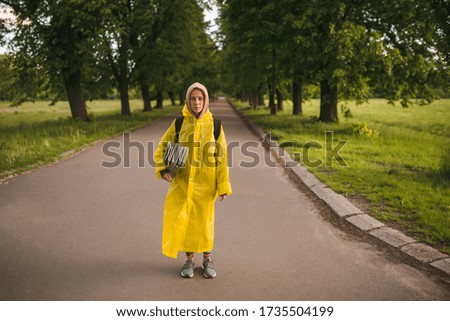 Beautiful young girl with green eyes stand in the green alley of a spring park with a yoga mat before meditation to escape isolation through  a digital detox