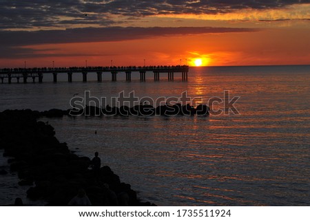 people silhouette standing on wooden pier at the sea with beautiful bloody sunset. A long exposure golden sunset view of a wooden jetty along the coast with calm sea.
