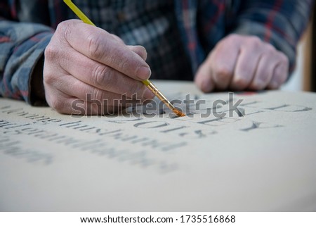 Stonemason painting stencilled letters in granite memorial Royalty-Free Stock Photo #1735516868