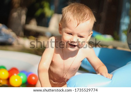 Laughing boy in the children's pool. Sunny summer mood picture. A cheerful kid plays in the pool with drops of water under bright sunshine.