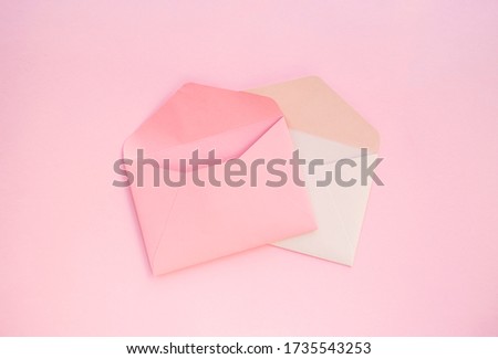 Two paper pink and white envelopes on pastel pink background.