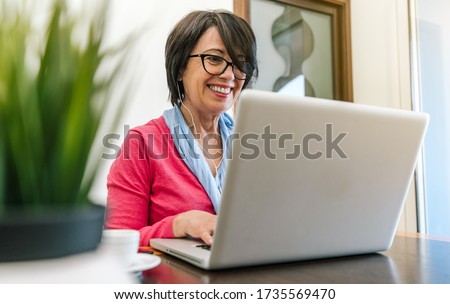 Senior older woman working with laptop computer on the table at home indoor. Old mature people and technology concept Royalty-Free Stock Photo #1735569470