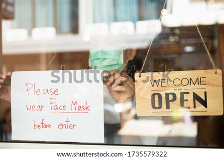 Asian cafe or restaurant shop owner woman attaching request customer to wear face mask before enter cafe sign board at entrance door for prevent corona virus infection after lock down from pandemic.