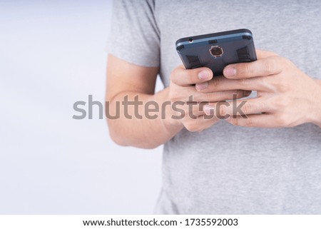 Yong man wearing grey shirt holding smartphone on white background. Technology concept.
