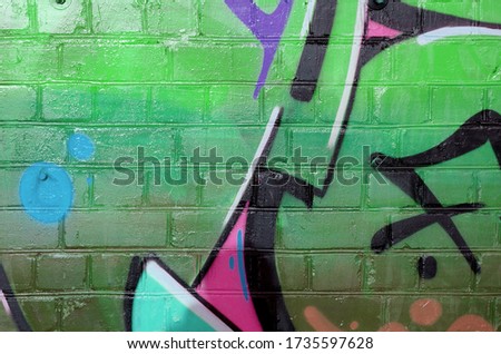 Abstract colorful fragment of graffiti paintings on old brick wall in green colors. Street art composition with parts of unwritten letters and multicolored stains. Subcultural background