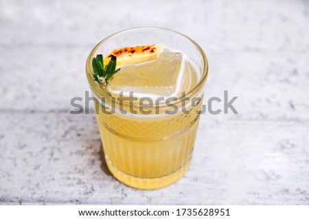 Fresh penicillin alcoholic cocktail with a slice of orange and ice cubes. An alcoholic Scottish penicillin cocktail with lemon, ginger sprig of rosemary and burnt sugar. light white gray background Royalty-Free Stock Photo #1735628951