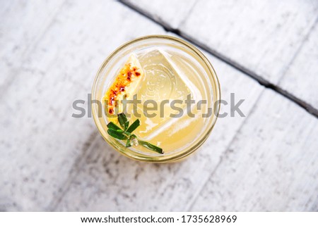 Fresh penicillin alcoholic cocktail with a slice of orange and ice cubes. An alcoholic Scottish penicillin cocktail with lemon, ginger sprig of rosemary and burnt sugar. light white gray background Royalty-Free Stock Photo #1735628969