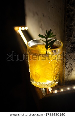 Fresh penicillin alcoholic cocktail with a slice of orange and ice cubes.Scottish penicillin cocktail with lemon, ginger sprig of rosemary and burnt sugar. dark background with lights and wooden table Royalty-Free Stock Photo #1735630160