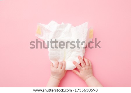 Baby hands touching white diaper on light pink table background. Pastel color. Closeup. Point of view shot. Royalty-Free Stock Photo #1735630598