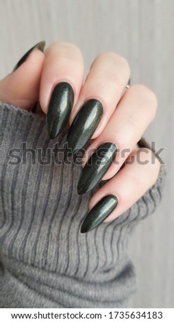 Female hand with long nails and a green manicure holds a bottle of nail polish