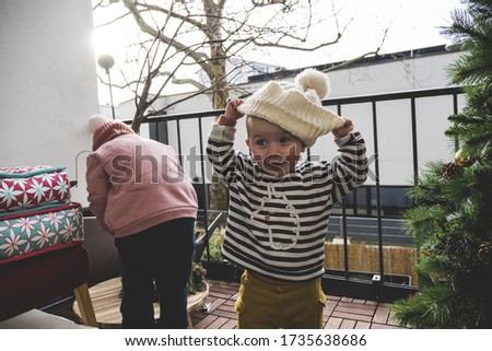 A cute little baby putting on a white knitted winter hat near the Christmas tree