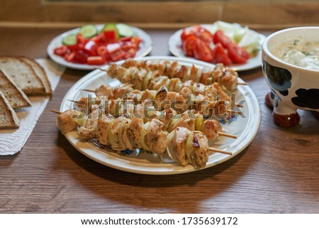 Close up picture of the table with healthy greek style dish consist from grilled chicken breast skewers  , chopped fresh vegetables, onion, potatoes, cucumber and sweet red pepper and slices of bread.
