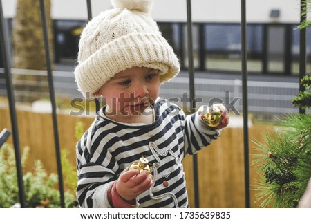 A shallow focus shot of a little baby in a knitted hat decorating the Christmas tree