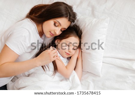 Happy young mother hugs her little daughter in bed, a view from above. mother and daughter rest in bed at home. Good morning!