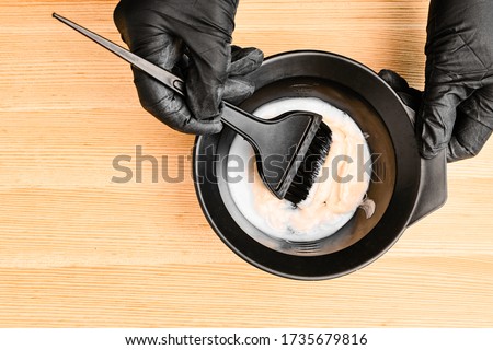 Tools for hair dyeing in hairdresser hands on the wooden background. Colouring of hair at home Royalty-Free Stock Photo #1735679816