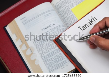 A student of Tanakh writing on a notebook with a bible opened to the book of the prophet Nehemiah. Royalty-Free Stock Photo #1735688390