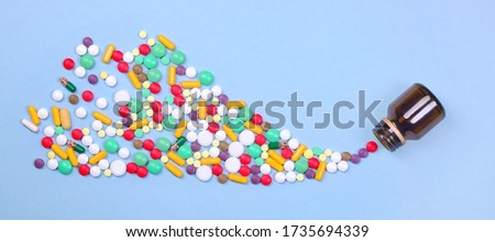 Pills and capsules of different colors fly out of a glass jar on a pale blue background. Medical concept. Flat lay. Wide format banner.  Royalty-Free Stock Photo #1735694339