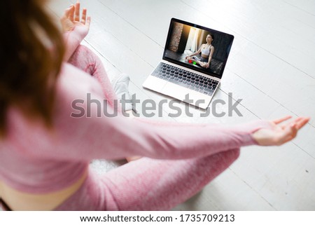Close-up of a laptop screen with a video tutorial on yoga and a girl in a sports form meditating in a lotus position.